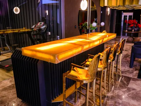Luminous golden stone is used for the bar counter and backdrop, alongside dark cabinetry and warm timber details.