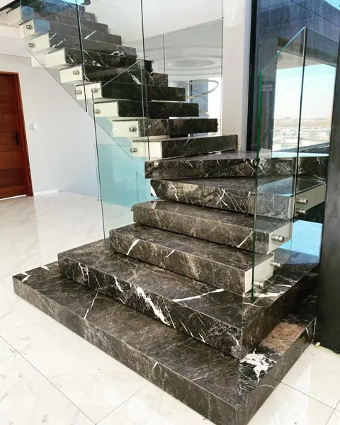 Dark stone with light veining is used for the stair treads and landings, alongside glass balustrades and generous daylight.