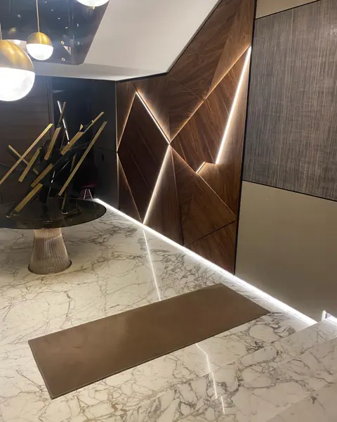 Rich brown veined stone is used for the stair treads and landings, alongside vertical timber detailing and warm concealed lighting.
