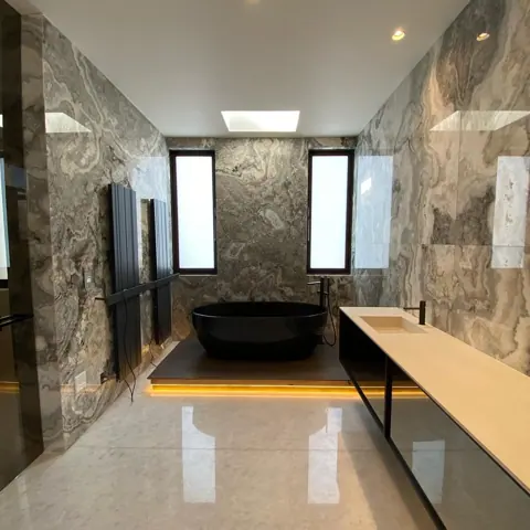 Grey veined stone is used for the bathroom walls and floor, alongside clean architectural lines and contemporary fittings.