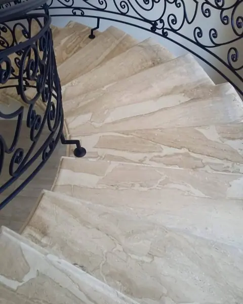 Pale veined stone is used for the stair treads and landings, alongside decorative metal balustrades and a bright stairwell.