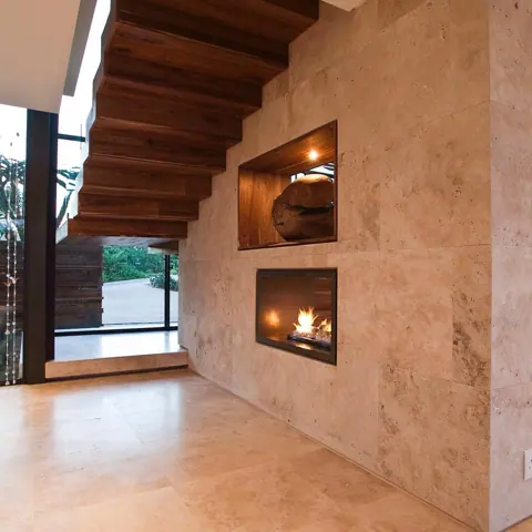 Warm beige natural stone is used for the fireplace surround, alongside timber beams and a sheltered entertaining area.
