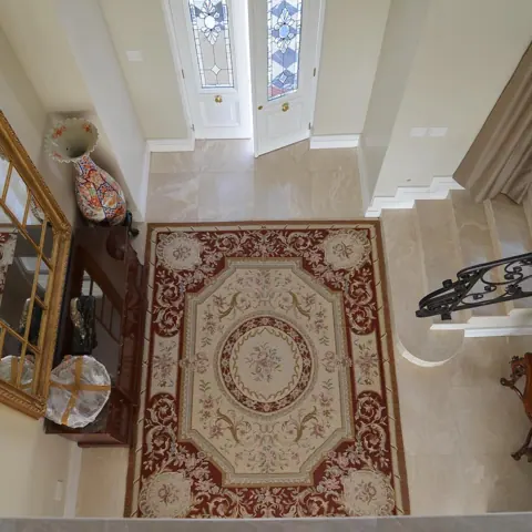 Warm beige natural stone is used for the entrance floor and architectural details, alongside classical mouldings and decorative lighting.
