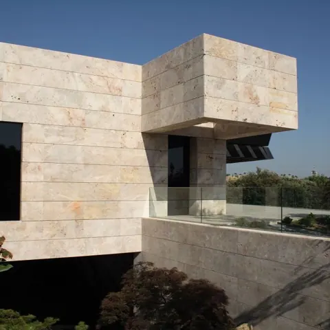 Warm beige natural stone is used for the exterior walls and entrance, alongside clean architectural lines and contemporary fittings.