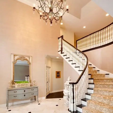 Soft cream stone is used for the stair treads and landings, alongside decorative metal balustrades and a bright stairwell. A dark handrail follows the curve of the white stairway.