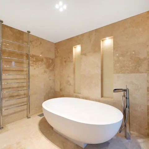 Warm beige natural stone is used for the bathroom walls and floor, alongside honey coloured walls and a freestanding bath.
