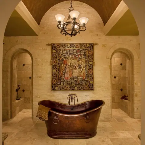 Warm beige natural stone is used for the bathroom walls and floor, alongside arched openings and a traditional interior palette.