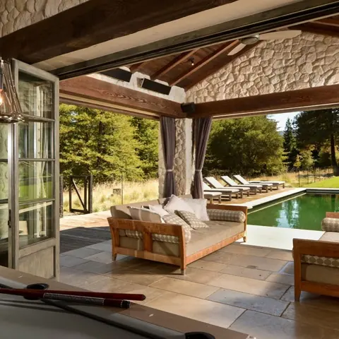 Warm beige natural stone is used for the terrace paving, alongside timber beams and a sheltered entertaining area.